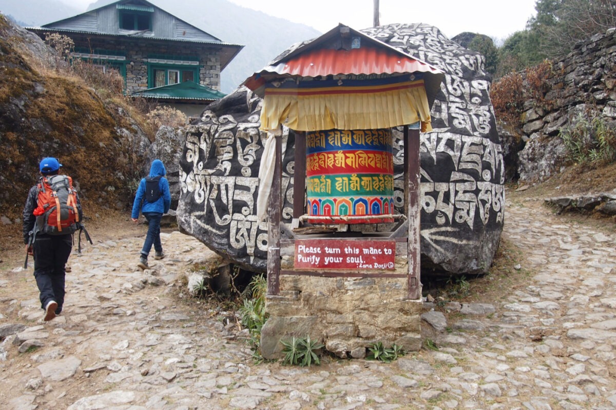 Child and sherpa trekking in Nepal, passing a mani wall on the left hand side.