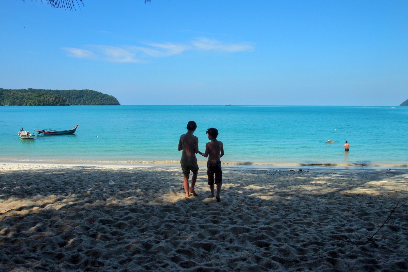 Children standing on sandy beach with beautiful blue water and palm trees in Malaysia